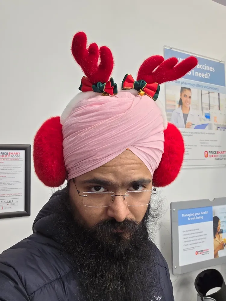 Daljot Singh looking deadpan at the camera wearing red reindeer antlers and fluffy red earmuffs over a pink turban.