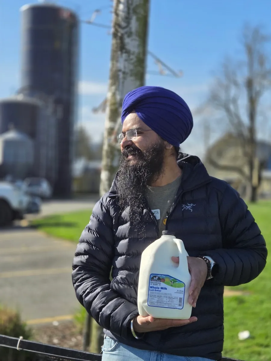 Daljot Singh holding a jug of whole milk outside a dairy farm, silos behind him.